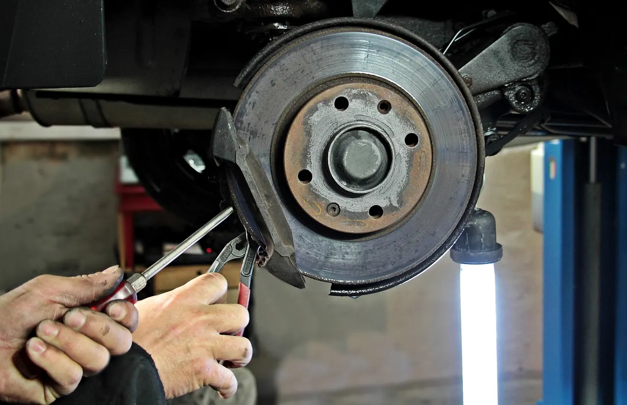 Hände arbeiten an einer Bremsscheibe unter einem angehobenen Auto